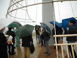 雨の中、県の担当者から説明を受ける参加者